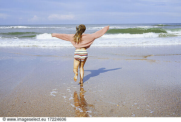 Teenager-Mädchen läuft am Strand Richtung Meer