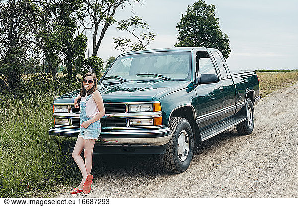 Teenager-Mädchen lehnt sich an einen grünen Lastwagen  der entlang einer unbefestigten Straße geparkt ist