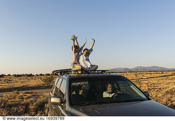 Teenager-Mädchen und ihr jüngerer Bruder oben auf SUV auf Wüstenstraße