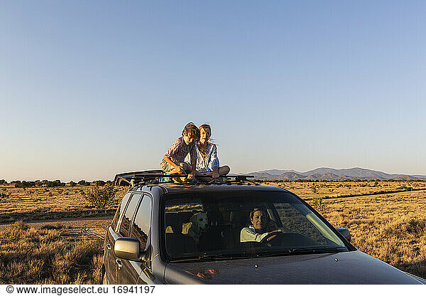 Teenager-Mädchen und ihr jüngerer Bruder oben auf SUV auf Wüstenstraße