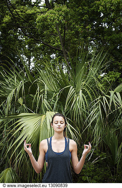 Teenager meditating in lotus position against plants