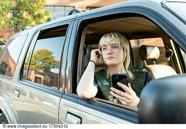 Teenager schaut aus dem Beifahrerfenster eines Autos und hält ein Handy in der Innenstadt