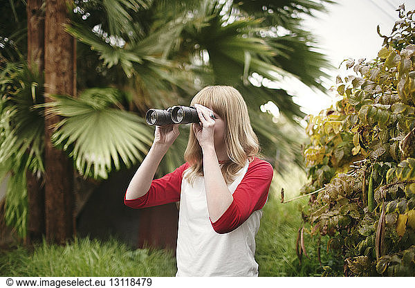 Teenager schaut durch ein Fernglas  während er im Park bei Pflanzen steht