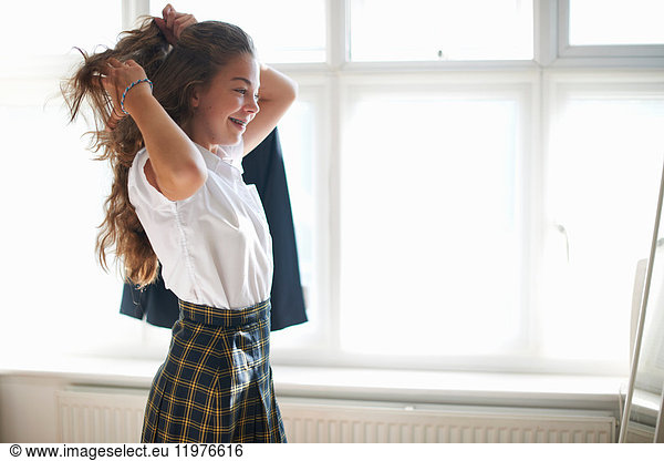 Teenager-Schulmädchen stylt langes Haar im Schlafzimmer