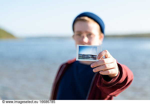 Teenager showing instant film photo to viewer with lake in background