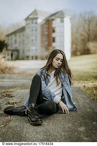 teenager sits on ground pavement looking sad thoughtful depressed