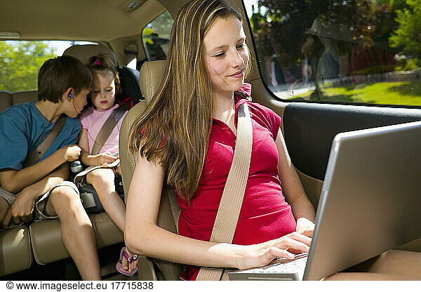 Teenager Using A Laptop With Siblings In The Background Playing With Electronics In A Mini Van  Bradford  Ontario