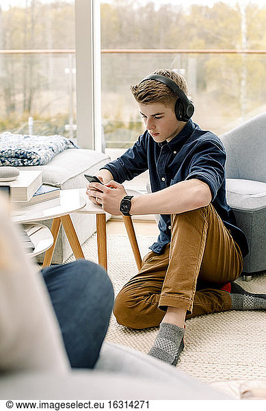 Teenager using mobile phone while sitting on floor at home