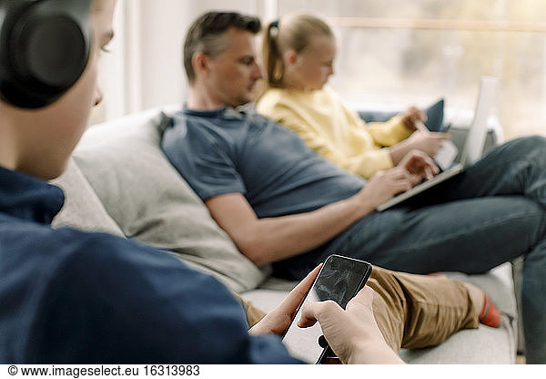 Teenager using smart phone while sitting on sofa with family