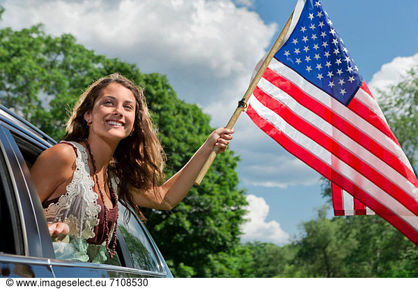 Teenagermädchen lehnt sich aus dem Autofenster und hält die amerikanische Flagge.