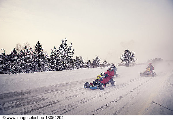 Teenagers racing on go-carts at snow covered field against sky