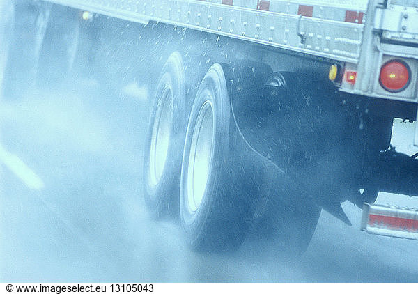 Teilansicht eines großen Lastkraftwagens  der unter gefährlichen Schnee- und Regenbedingungen auf einer Autobahn fährt.