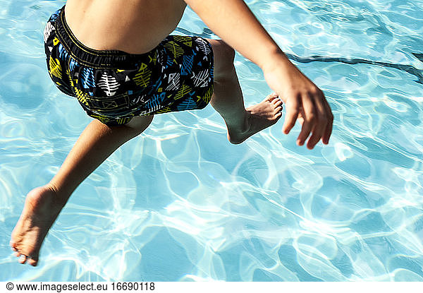 Teilansicht eines Jungen  der in ein Schwimmbecken springt.