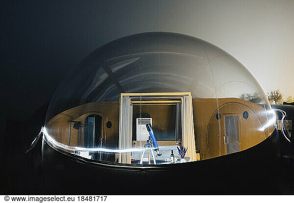 Telescope on tripod inside dome tent with light trails at night