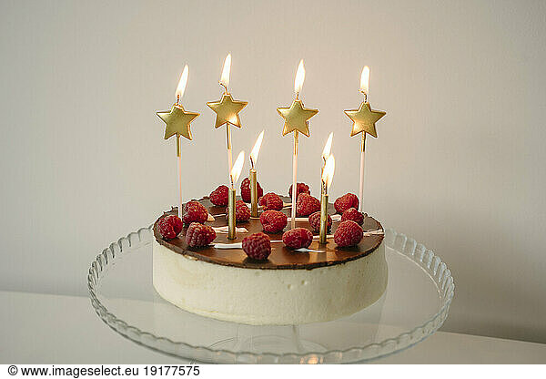 Tempting cake with burning candles on table in front of wall