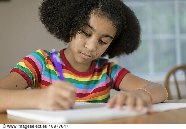 Ten year-old bi-racial girl doing homework at table