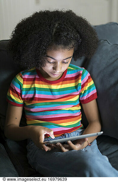 ten year-old bi-racial girl looking at ipad on sofa