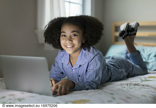 Ten year-old bi-racial girl working on apple laptop smiling at camera