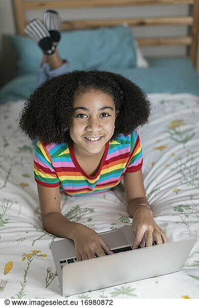 Ten year-old bi-racial girl working on her apple laptop and smiling