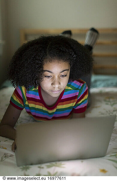 Ten year-old bi-racial girl working on her apple laptop  lying on bed