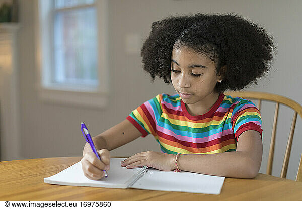 Ten year-old bi-racial girl writing in notebook at table