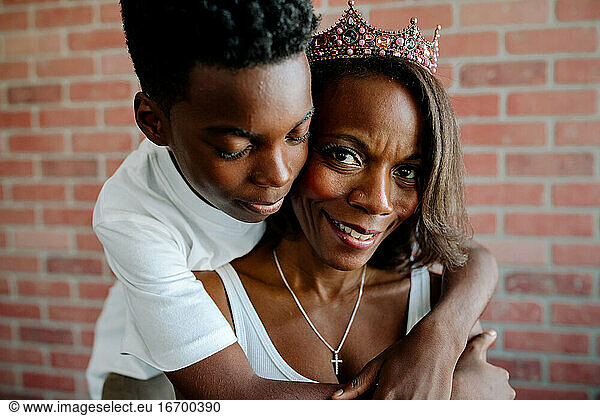 Tender preteen son hugging beautiful Black mom wearing tiara