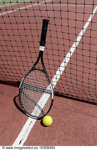 Tennis racket with ball by net in court during sunny day
