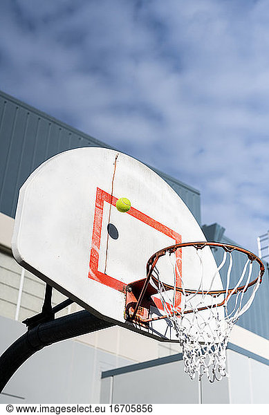 Tennisball trifft Rückwand auf Basketballkorb unter bewölktem Himmel