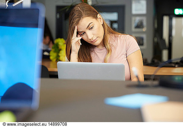 Tensed creative businesswoman looking at laptop while sitting in office