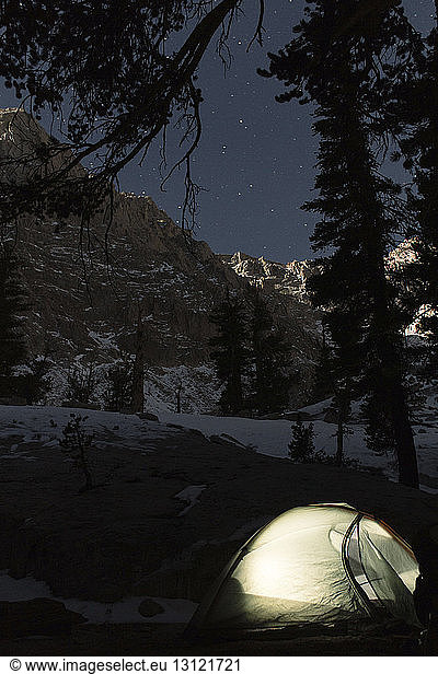 Tent on field against snowcapped mountains at night