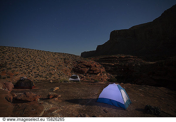 Tents illuminated by moonlight in a rugged desert environment at night
