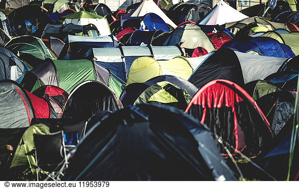 Tents on grass packed tightly together  pitched close together at an outdoor music festival in summer. A packed camping field.