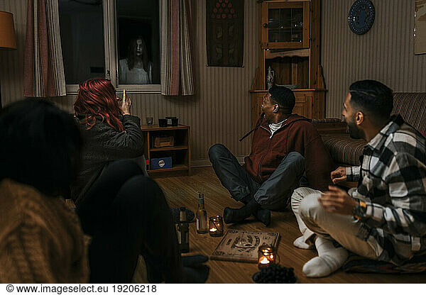 Terrified multiracial friends looking at ghost through window in log cabin