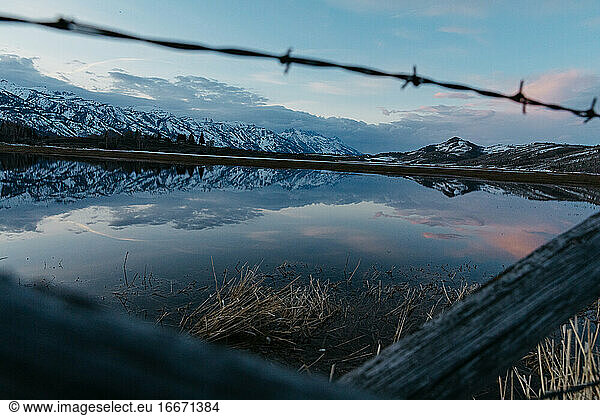 teton mountain range reflection through wire fence at flooded ranch