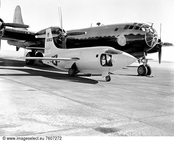 The Bell Aircraft Corporation X_1_2 sitting on the ramp at NACA High_ Speed Flight Research Station with the Boeing B_29 launch ship behind. The B_29 was fondly referred to as Fertile Myrtle. The painting near the nose depicts a stork carrying a bundle which is symbolic of the Mothership launching her babe X_1_2. The pilot access door is open to the cockpit of the X_1_2 aircraft.