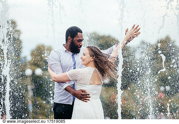 The couple of diverse people are dancing in a city fountain