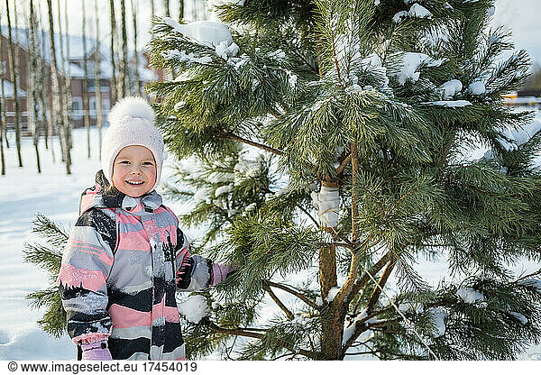 The cute girl standing by the tree and looking at the camera.