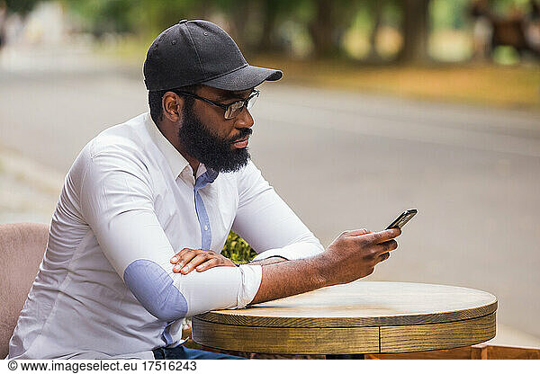 The fashionable young man with a smartphone in a street cafe