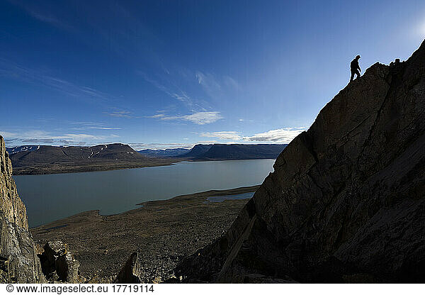 The figure of expedition team member climbing the cliffs searching for more caves with lake Centrum in the background.