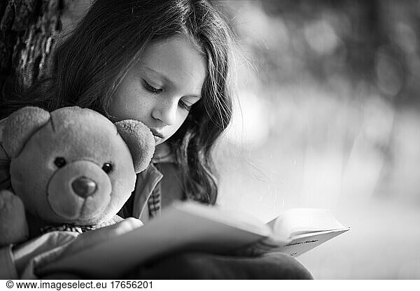 The girl is reading a story book with a teddy bear.