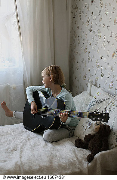 The girl plays a musical instrument and sings in a light room.