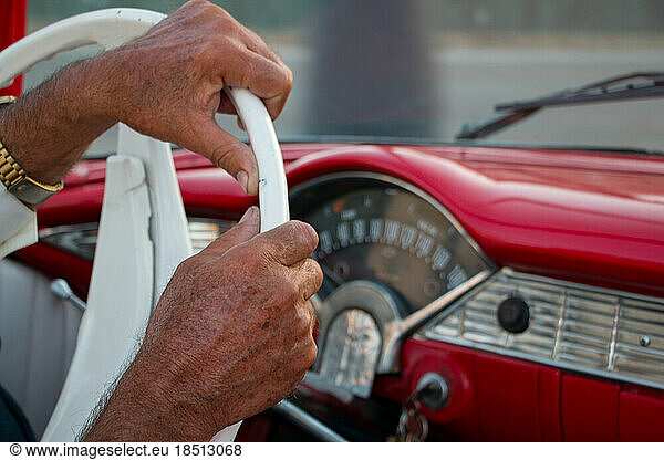 The hands of an older man at the wheel driving a classic car