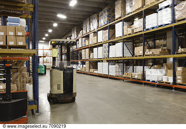 The interior of a storage unit or warehouse of a Correctional Facility. Shelves stacked high with goods ande supplies. A forklift truck.