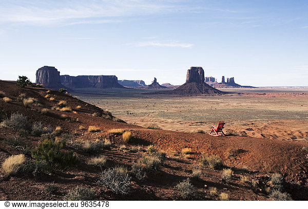 The landscape and eroded sandstone buttes and structure of Monument Valley. A single wooden chair.