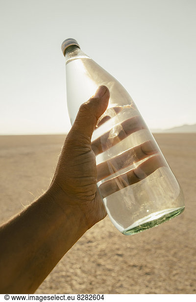The Landscape Of The Black Rock Desert In Nevada. A Man'S Hand Holding A Bottle Of Water. Filtered Mineral Water.