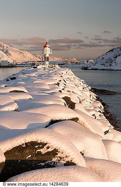 The lighthouse surrounded by snow frames the snowy peaks and the frozen sea Reine Nordland  Lofoten Islands  Norway  Europe