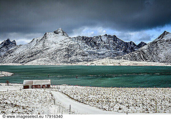 The Lofoten islands in snow  turquoise green water  small fishing village and houses on the shore under rising mountains.