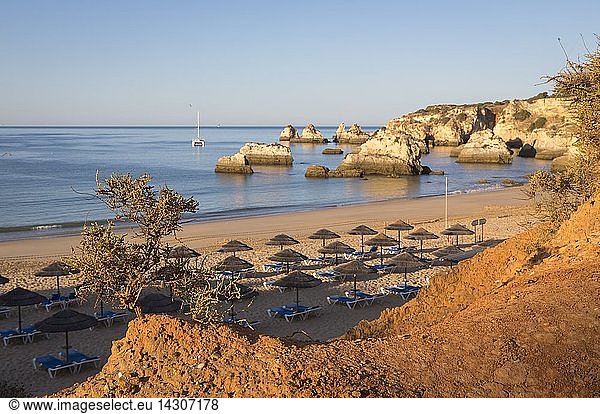The newly risen sun shines on cliffs and bathhouse of Praia do Alemao Portimao Algarve Faro District Portugal Europe