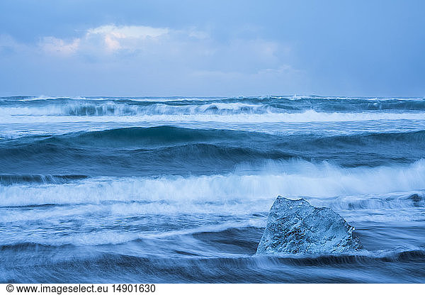 The ocean crashes around a chunk of ice on the South shore of Iceland near Jokulsarlon; Iceland