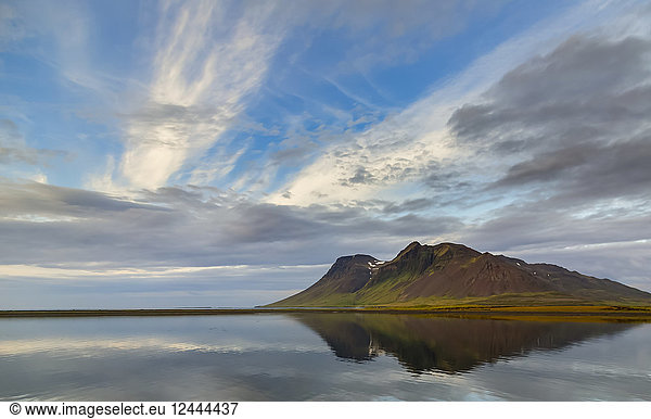 The rich volcanic earth creates bold colours on the mountain against the soft blue ocean and sky reflection in Western Iceland  Iceland
